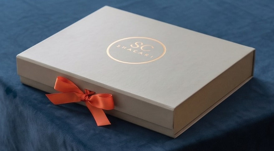 A Shacari gift box tied with a signature ribbon, resting on a navy bridge cloth